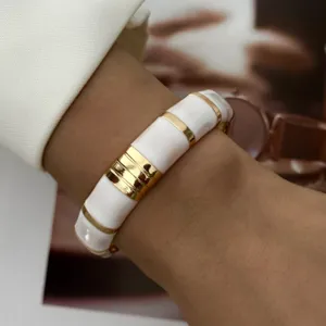 Detailansicht eines eleganten weißen Emaille-Armreifs mit goldenen Streifen am Handgelenk.