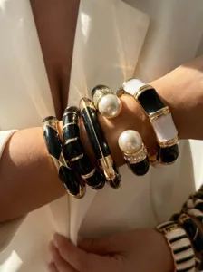 Close-up of stacked black and white enamel bangles with gold trim and pearls