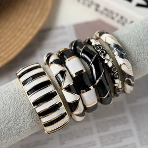 Close-up detail of retro black and white enamel bracelets with golden accents on a grey stand
