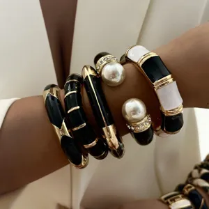 Detailed view of layered black and white enamel bracelets with faux pearls and gold finish