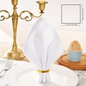 White cotton linen napkin detail view with gold ring on elegant dining table setting.