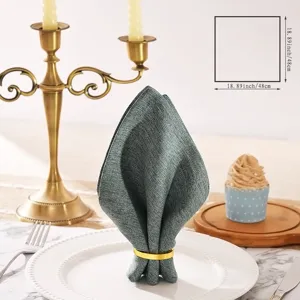 Detail view of elegant linen dinner napkin with gold ring in fine dining table setup scene.