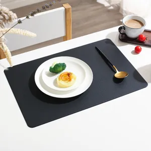 Detailed shot of black leather placemat on white table with elegant tableware setup.
