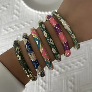 Detail view of ethnic enamel bangles featuring floral and evil eye designs on wrist.