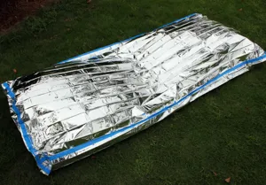 PE aluminum emergency thermal blanket detail view showing outdoor survival sleeping bag use.