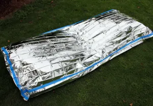 Detailed shot of PE aluminum foil emergency survival blanket spread out on green grass.