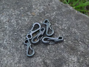 Detailaufnahme von Mini Metall Feder Karabiner Haken EDC Ausruestung auf Steinplatte.