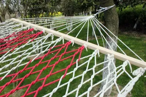 Detail van de geweven katoenen touwhangmat met rood witte net en houten spreidstokken.