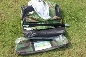 Detail view of camouflage camping tent components, showing folded fabric, mesh and poles.