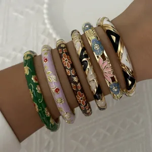 Close-up view of intricately designed floral enamel bangles stacked on a person's arm