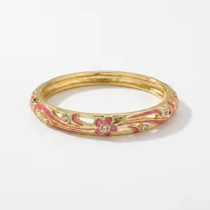 Elegant gold-plated enamel bangle with pink flower patterns and sparkling crystals.