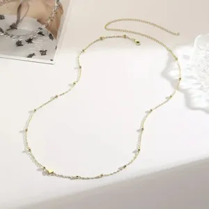 Detail view of a dainty gold-tone body chain with small beads and a sweet heart charm.