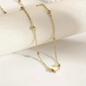 Detailed view of a minimalist gold body chain with small beads and a heart pendant