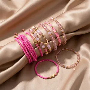 Nahaufnahme eines 10-teiligen rosa Herz-Perlenarmband-Sets auf champagnerfarbenem Satin.
