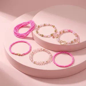 Nahaufnahme eines rosa Perlenarmband-Sets mit goldenem Herzanhänger auf rosa Podesten