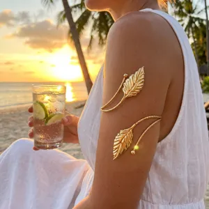 Detail of a gold leaf spiral arm cuff worn on the arm against a sunset beach background.