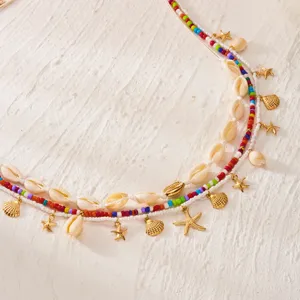 Dettaglio di una catena da vita da spiaggia con perline colorate, conchiglie e stelle marine oro.