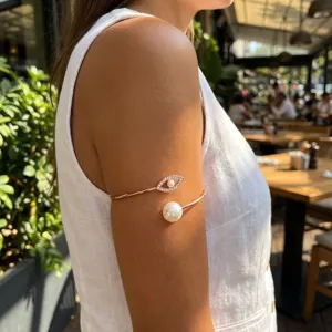 Detail view of rose gold spiral arm cuff with pearl and evil eye on model's arm