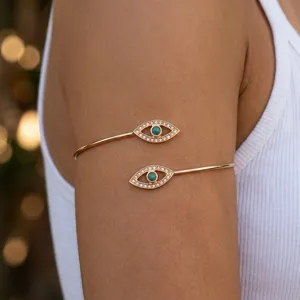 Detailed view of an ethnic gold spiral arm cuff with turquoise evil eye motifs.