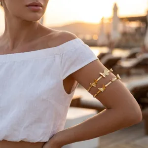 Detailed view of golden butterfly open arm cuffs worn by a model at sunset beach