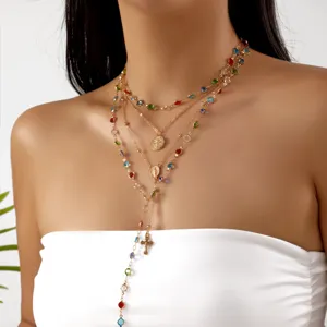 Close-up of a layered gold necklace featuring colorful rhinestones and a cross pendant