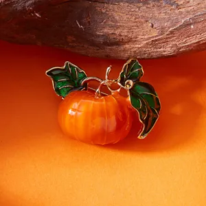 Detail einer glänzenden Emaille-Kürbis-Brosche mit grünen Blättern auf goldenem Rahmen.