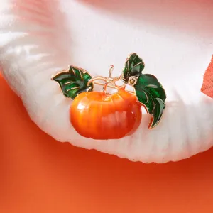 Makroansicht einer orangefarbenen Emaille-Kürbis-Brosche mit grünen Blättern.