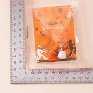 Primer plano de pendientes de Halloween con colgantes de calabaza y fantasma sobre una regla.
