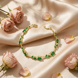 Detail of golden bracelet with green leaf-shaped crystals on champagne satin fabric.