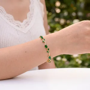 Elegant gold plated bracelet with sparkling green petal leaves worn on a delicate wrist