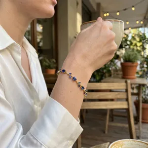Elegant gold bracelet with blue leaf-shaped gems worn by a model in a cozy cafe