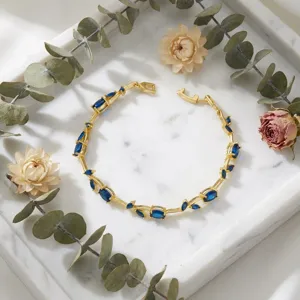 Detailed shot of an elegant gold-plated bracelet with blue leaf gems on white marble