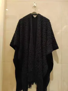 Gedetailleerd uitzicht op een zwarte gebreide poncho sjaal, met opengewerkte patronen voor dames.