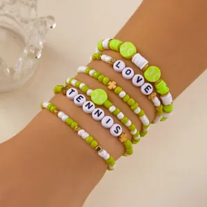 Close-up of lime green Tennis and Love beaded charm bracelets set on a person's wrist