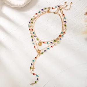 Detailed view of layered gold necklace with colorful rhinestones and cross pendant charm.