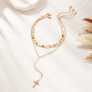 Detailed view of layered gold necklace with colorful rhinestones and cross pendant.