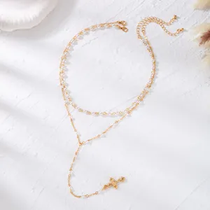 Close-up of a double-layered gold chain necklace with pearls and a cross pendant