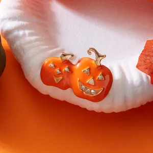 Nahaufnahme von orangefarbenen Emaille-Kürbis-Broschen mit Strasssteinen auf weißem Sockel.