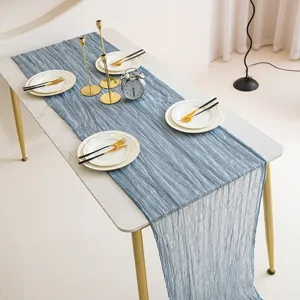 Detailed view of the blue-grey cheesecloth table runner styled on a dining table with plates and candles.