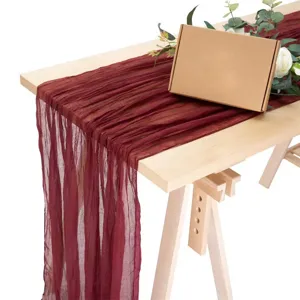 Detalle de camino de mesa de gasa burdeos que muestra un tul suave drapeado en madera.