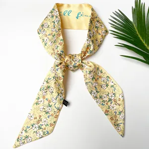 Detailopname van een gele zijden twilly sjaal met bloemenprint en een elegante labeltag.