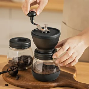Close-up detail view of a manual glass coffee grinder showing the hand crank mechanism in use.
