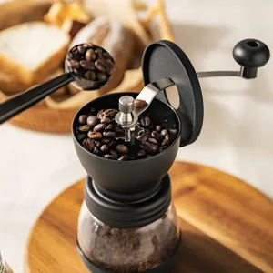 Manual coffee grinder detail shot showing glass jar, stainless steel crank and fresh coffee beans.