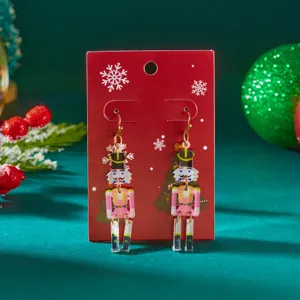 Festive pink Nutcracker soldier acrylic drop earrings displayed on a red Christmas card.