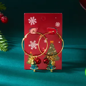Detail view of festive Christmas tree and bell charms on gold hoop earrings for women.