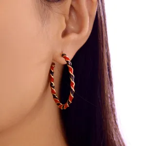 Detailed close-up view of festive red and black twisted enamel hoop earrings worn on ear