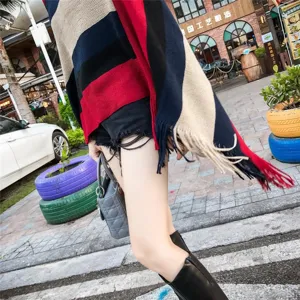 Detailed view of a striped knit poncho with fringe tassels in an outdoor setting