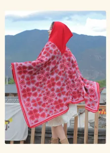 Rückansicht eines roten Ethno-Strickponchos mit Kapuze und Herzmuster vor Bergen