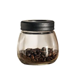 Glass coffee bean storage jar detail view, transparent container with black lid holding beans.