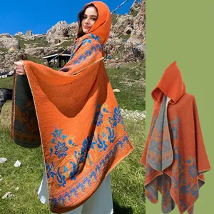 Vibrant orange hooded knitted poncho with intricate blue floral jacquard patterns.